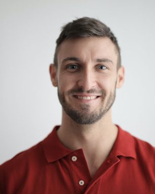 a man in a red shirt smiling at the camera.